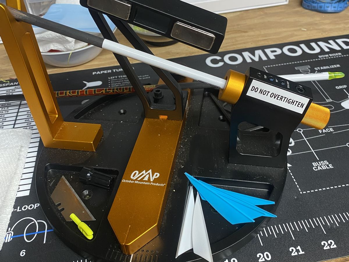 An arrow shaft clamped in a fletching jig, with blue and white vanes ready to install
