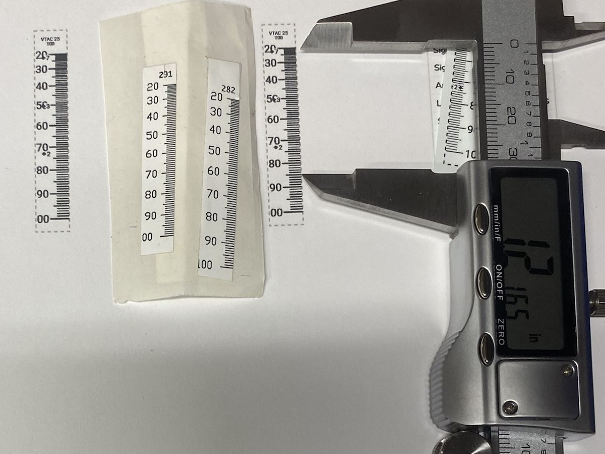 Printed sight tapes on a workbench beside a digital caliper