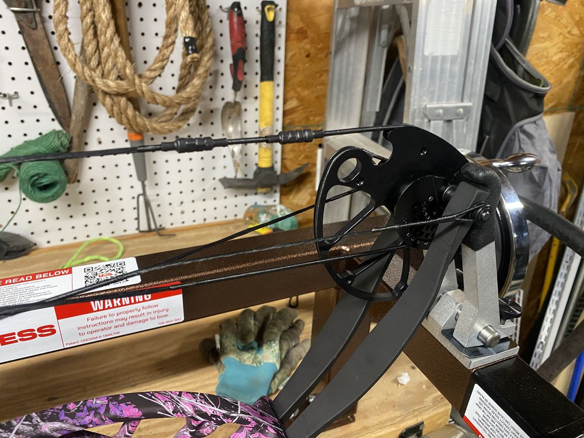 A compound bow's cam, string and cables in a bow press at the shop